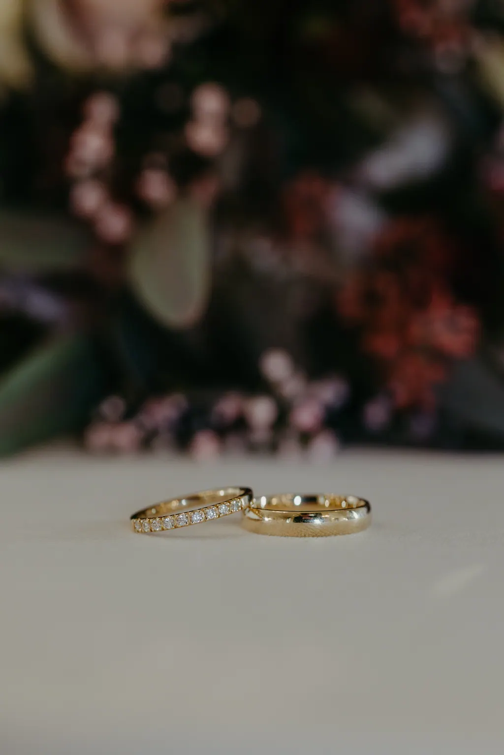 Zwei goldene Eheringe auf weißem Tisch vor unscharfen Blüten