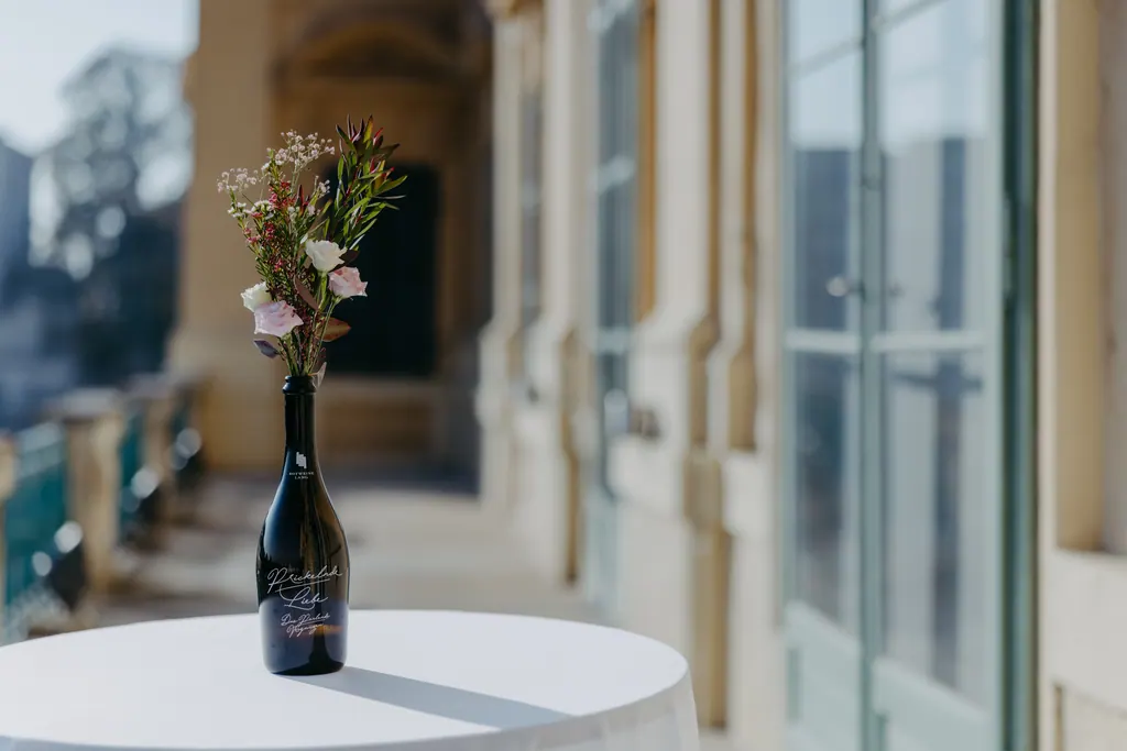 Stehtisch mit Blumen in einer Flasche in der hellen Galerie mit hohen Fenstern