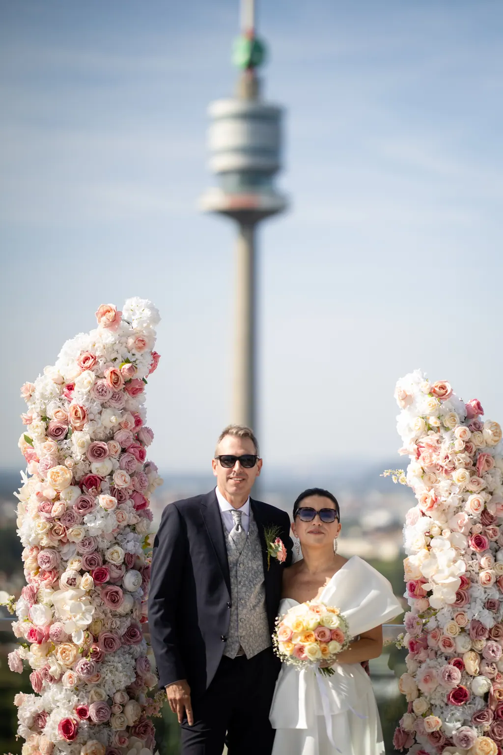 Brautpaar zwischen Blumensäulen, dahinter der Donauturm