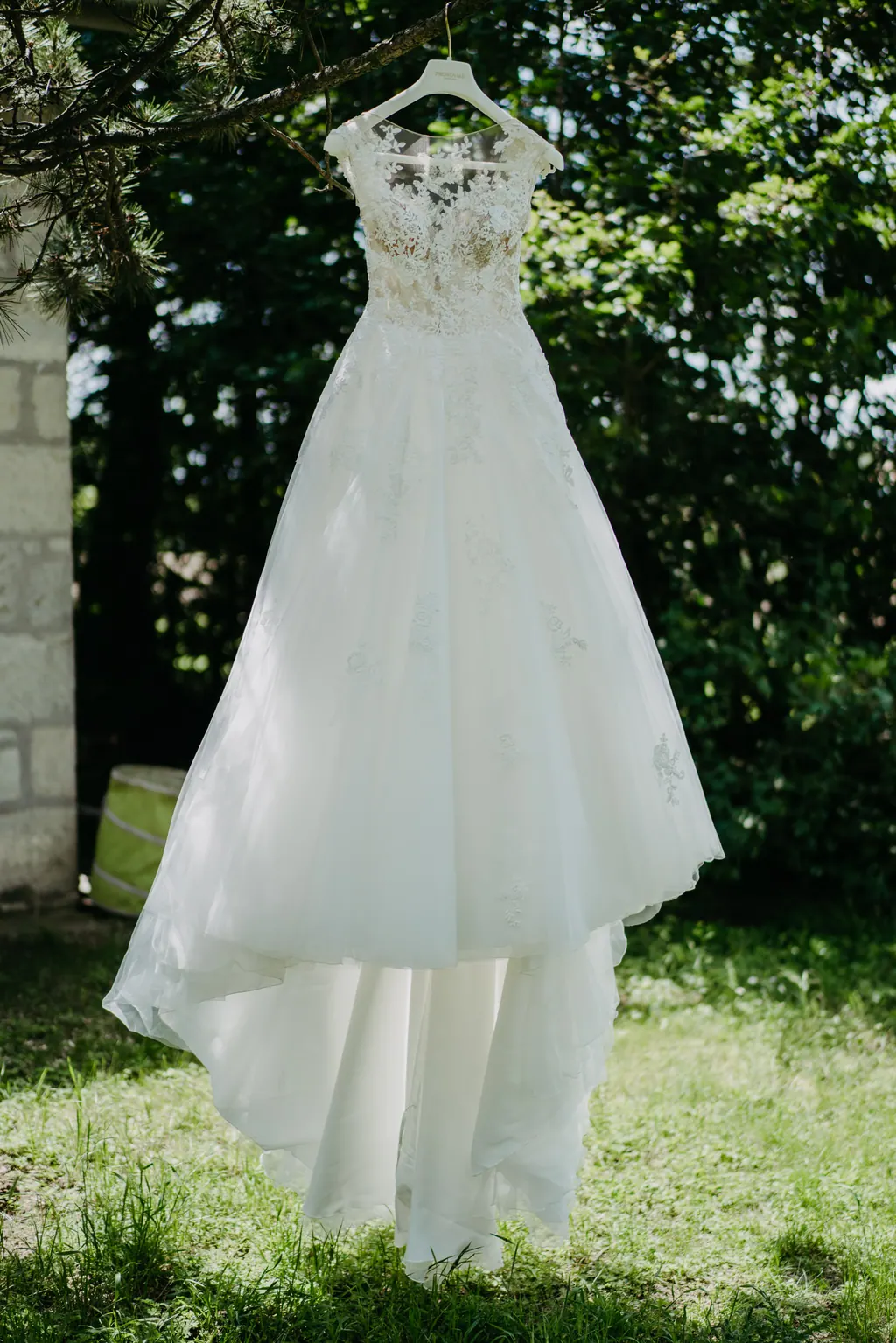 Brautkleid mit Spitzenoberteil hängt an einem Baum im Garten
