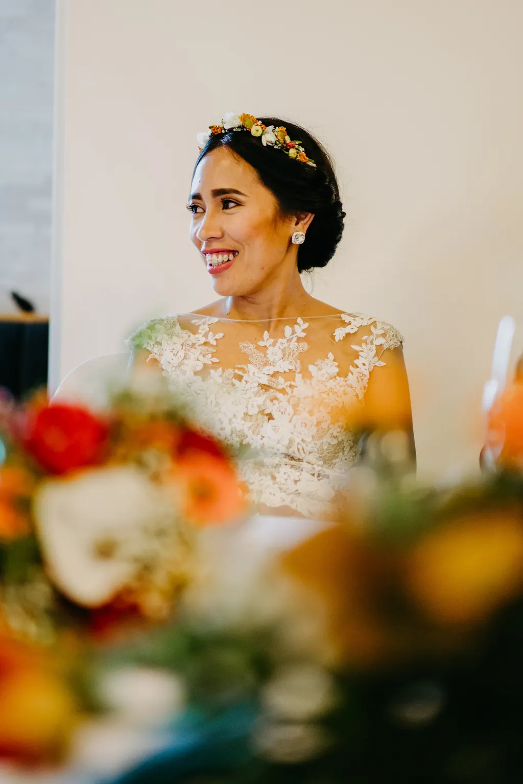 Braut mit Blumenkranz lacht bei der Feier hinter dem Tischschmuck