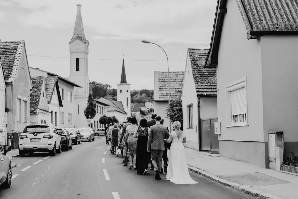 Hochzeitszug geht die Dorfstraße entlang zur Kirche, Schwarzweißaufnahme