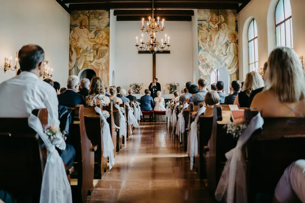 Blick durch den Mittelgang einer hellen Kirche mit Wandbildern zum Altar
