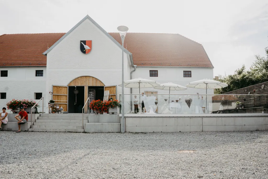 Weißer Gutshof mit Holztor, Gemeindewappen und Terrasse mit Sonnenschirmen