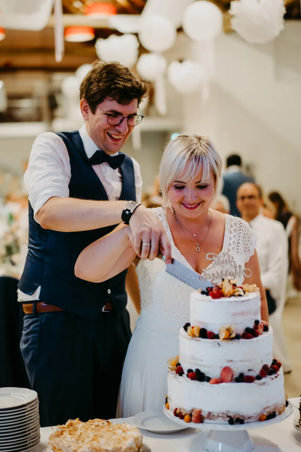 Brautpaar schneidet lachend die Torte mit Beeren an