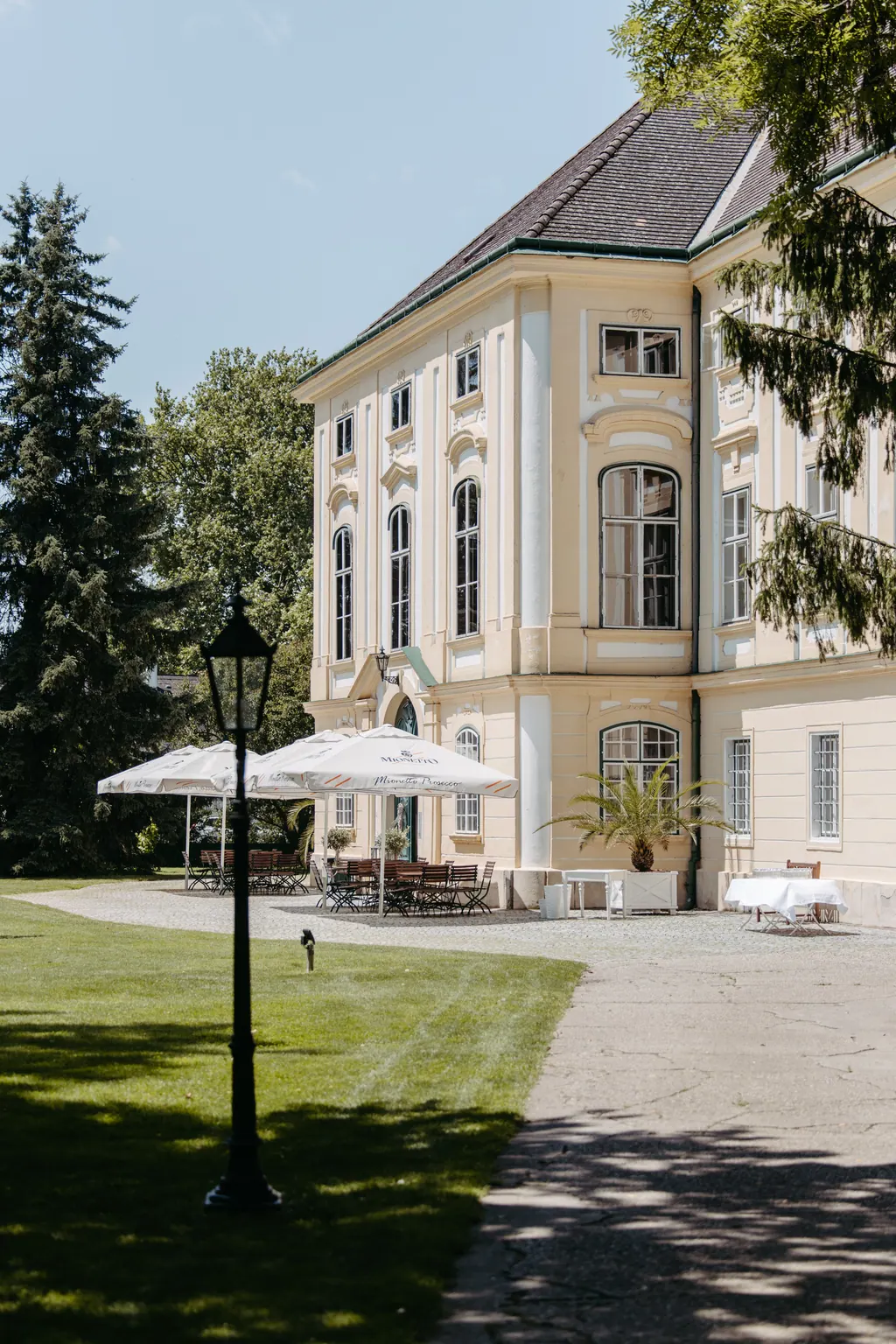 Barockfassade des Schlosses mit Parkweg, Laterne und Sonnenschirmen im Sommerlicht