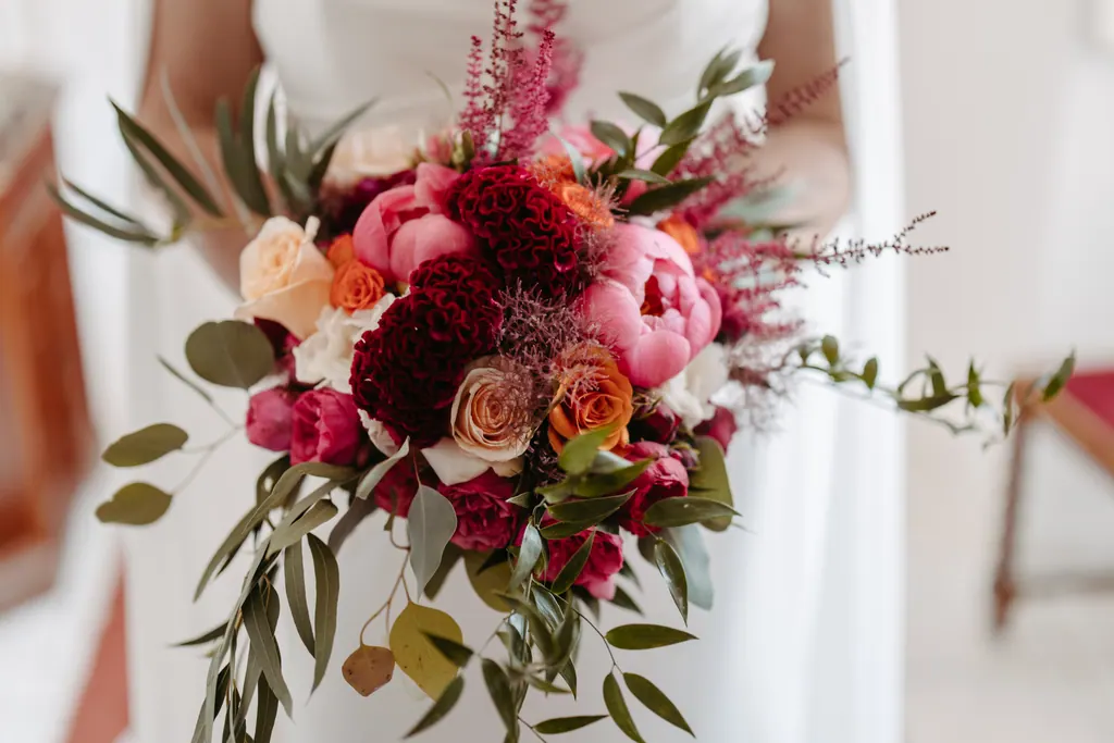 Brautstrauß aus Pfingstrosen, Rosen und Olivenzweigen vor dem weißen Kleid