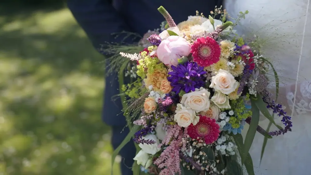 Bunter Brautstrauß mit Rosen, Gerbera und Gräsern in der Hand des Brautpaars