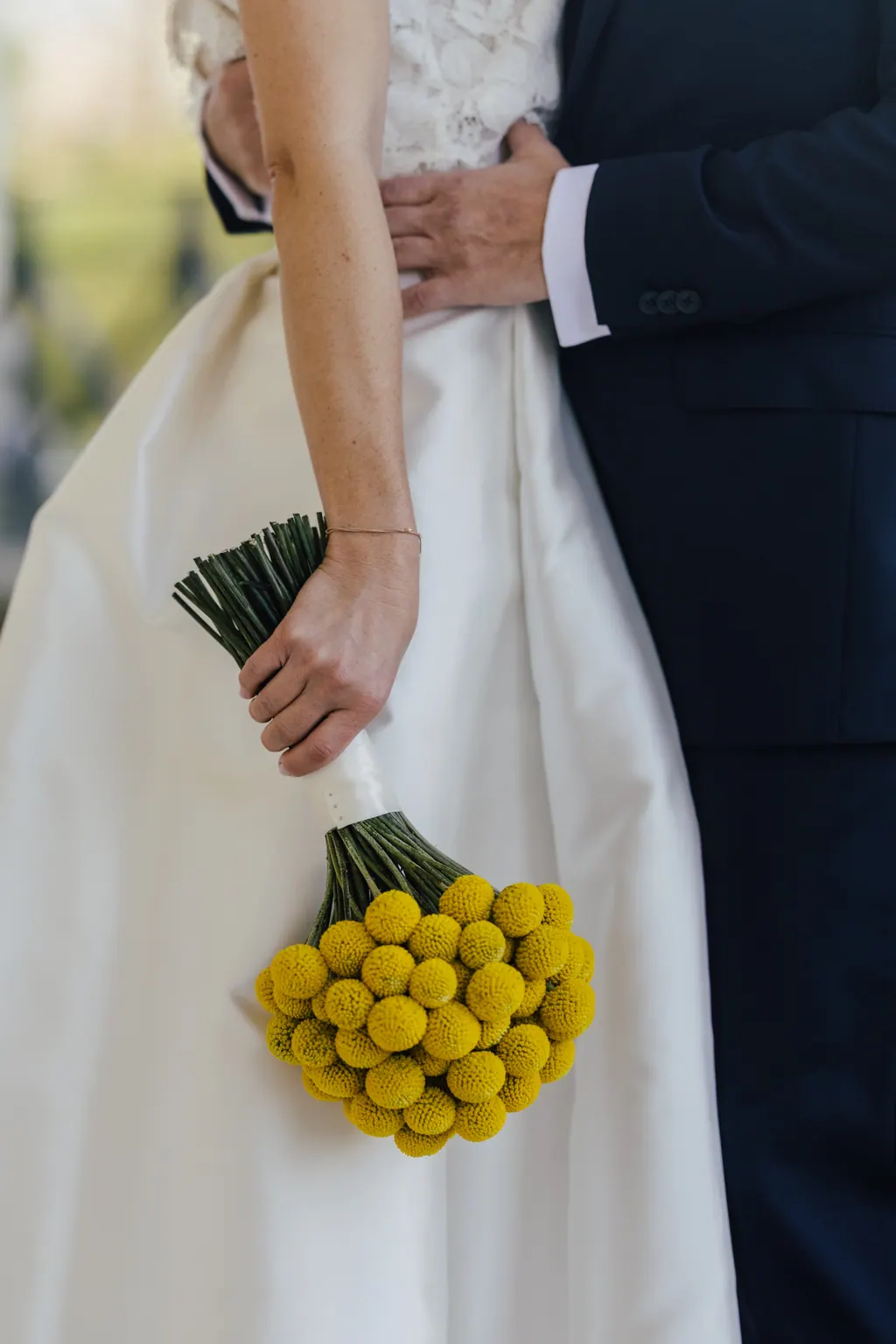 Gelber Kugelblumenstrauß in der Hand der Braut vor dem weißen Rock