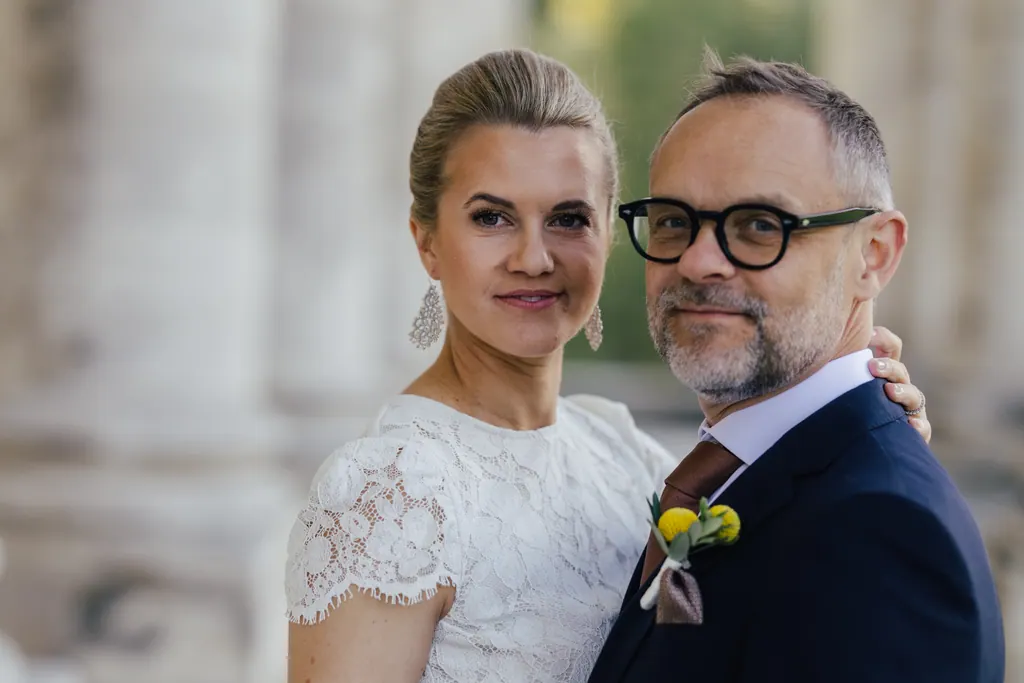 Brautpaar Wange an Wange blickt ruhig in die Kamera vor hellen Säulen