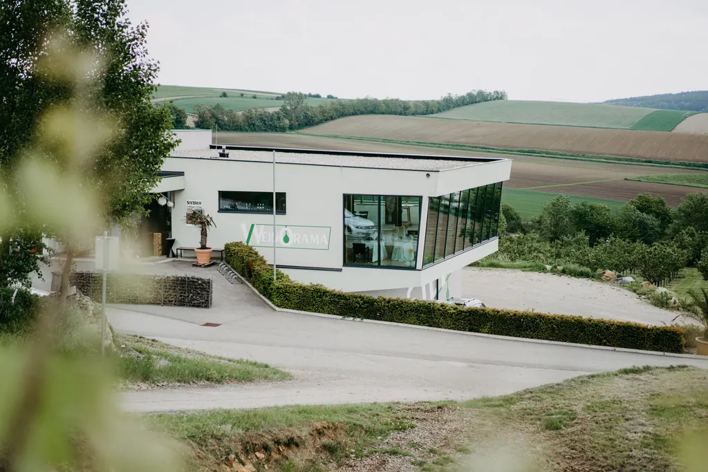 Modernes Weingut mit großen Glasfenstern über sanften Hügeln und Feldern