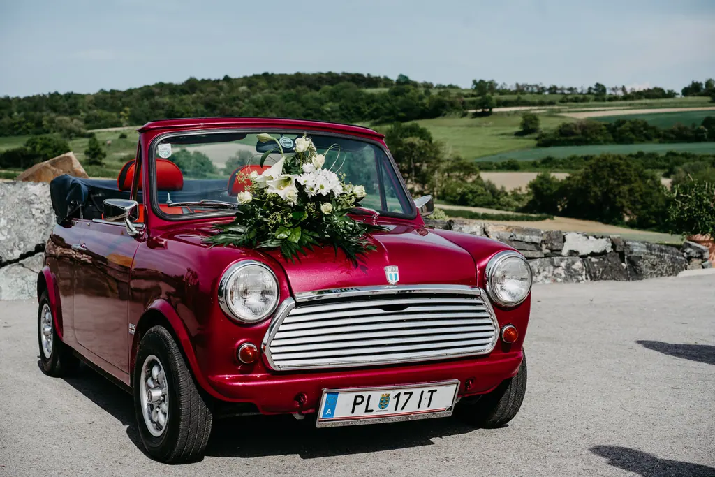 Rotes Mini-Cabrio mit Blumenschmuck vor hügeliger Landschaft
