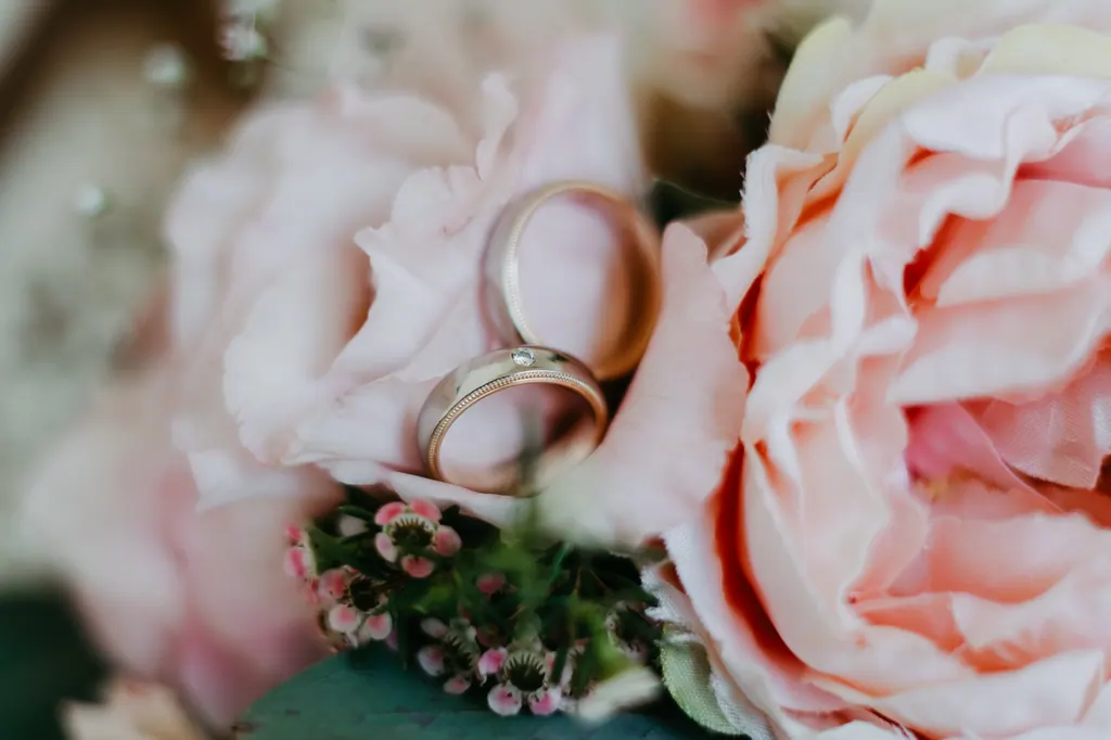 Eheringe liegen zwischen rosa Rosen im Brautstrauß