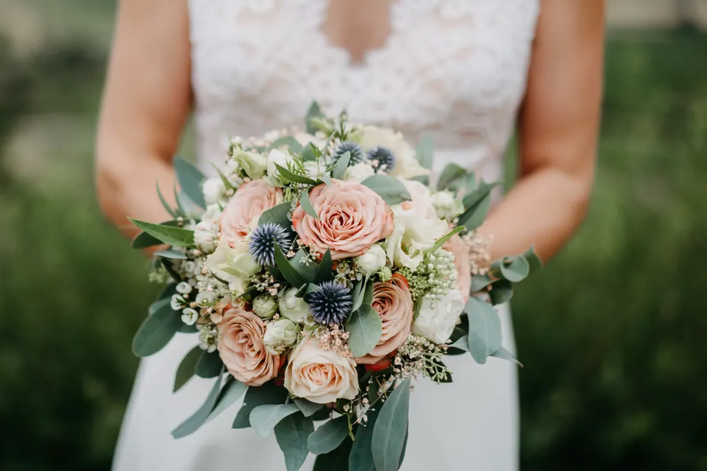 Brautstrauß aus Apricot-Rosen, Disteln und Eukalyptus vor dem Kleid