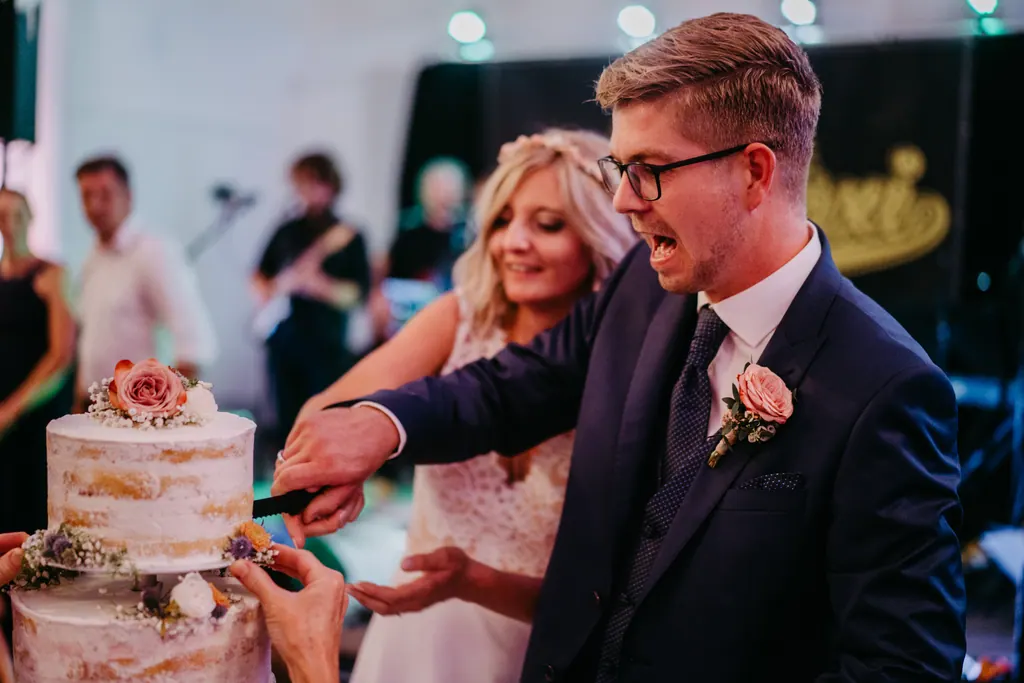 Brautpaar schneidet lachend die Hochzeitstorte an