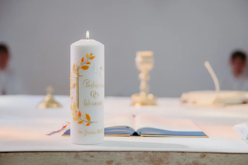 Brennende Hochzeitskerze mit goldenem Zweig neben Kelch auf dem Altar