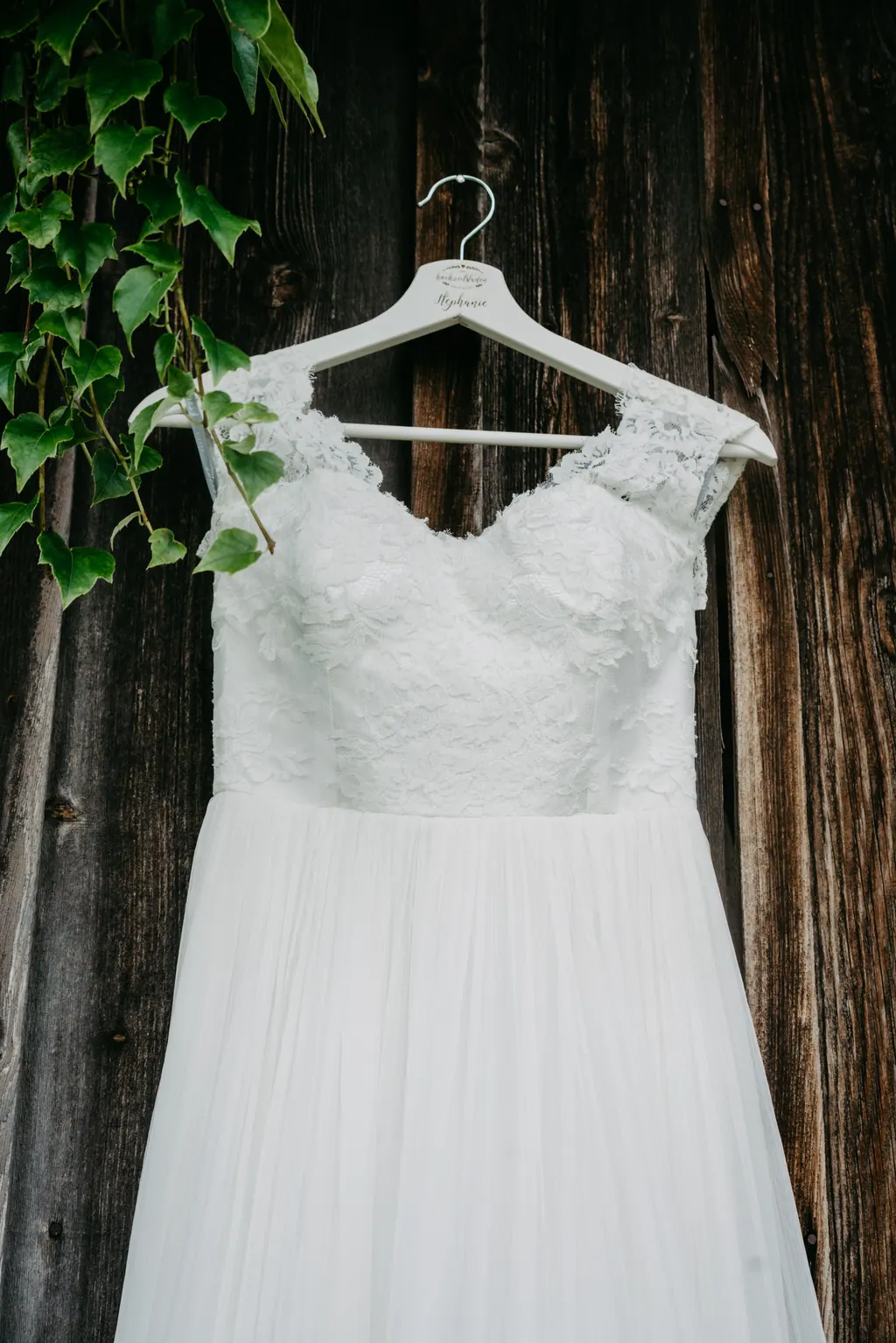 Brautkleid mit Spitze hängt an einer alten Holzwand mit Efeu