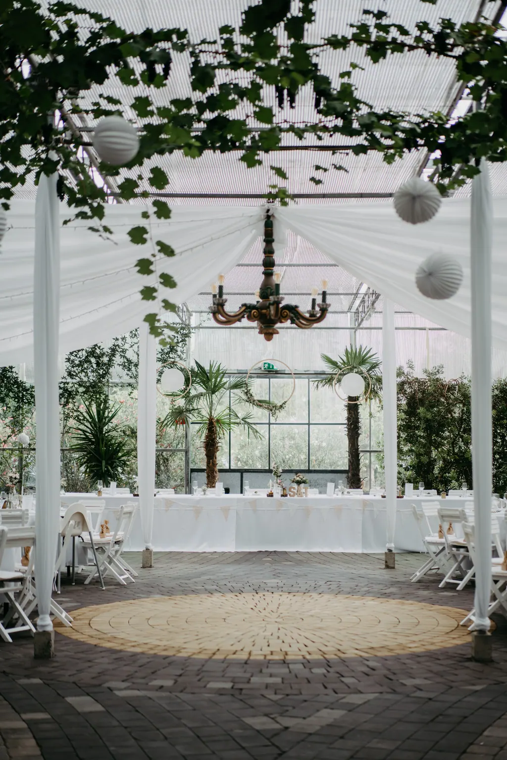 Glashaus mit Kronleuchter, Lampions und Palmen, festlich gedeckt