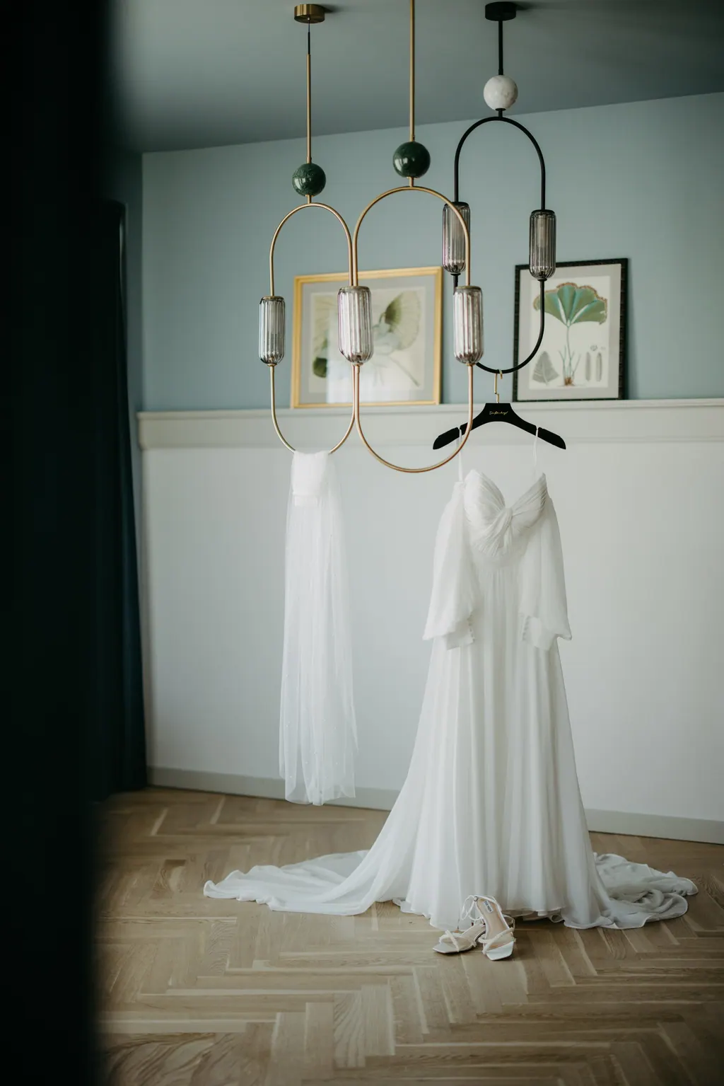 Brautkleid hängt unter einer Messingleuchte im Hotelzimmer