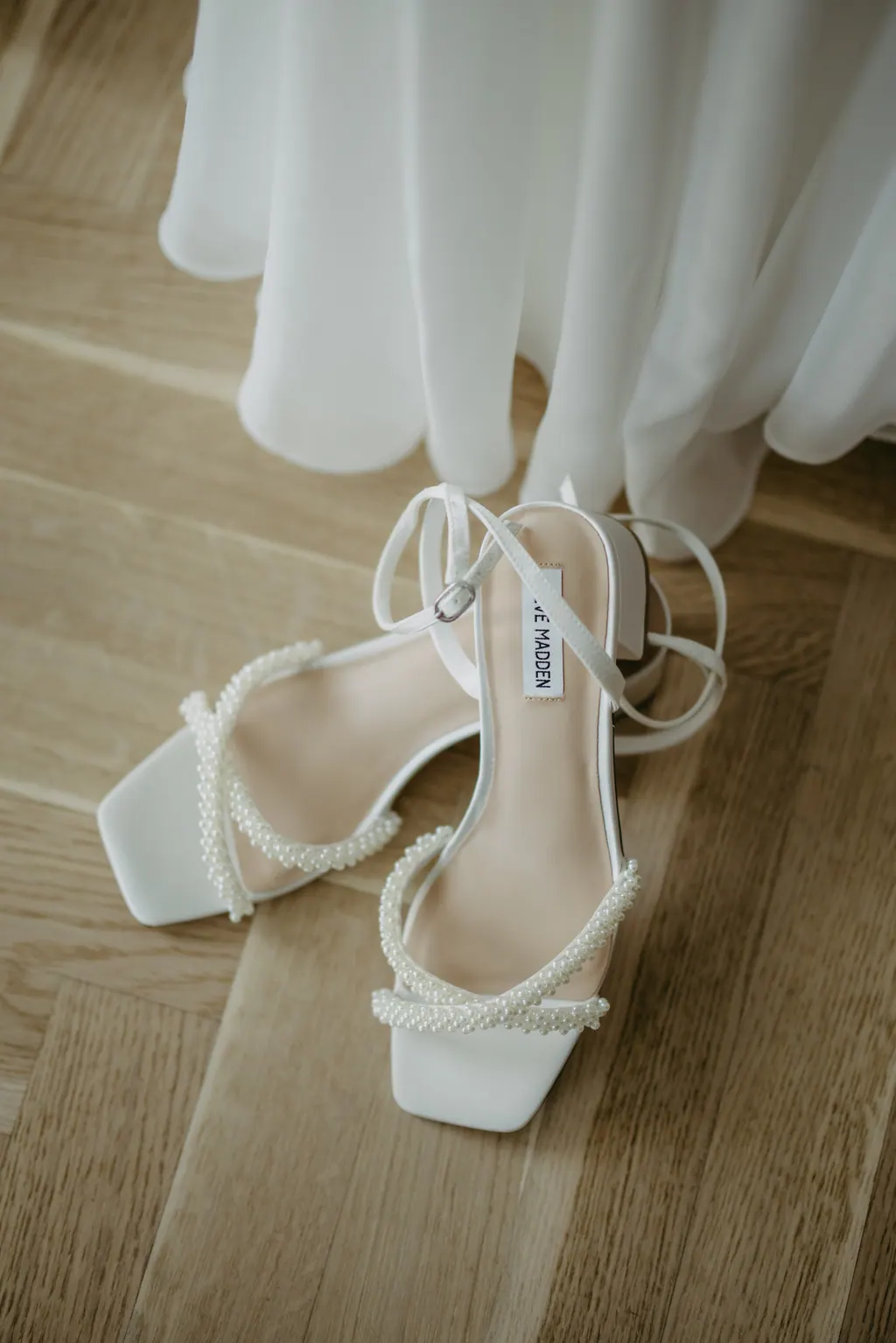 Weiße Brautsandalen mit Perlenriemen auf Holzparkett