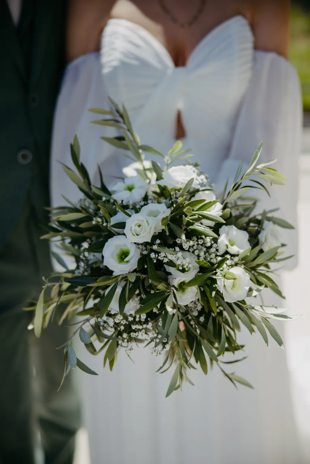 Brautstrauß aus weißen Rosen und Olivenzweigen vor dem Kleid