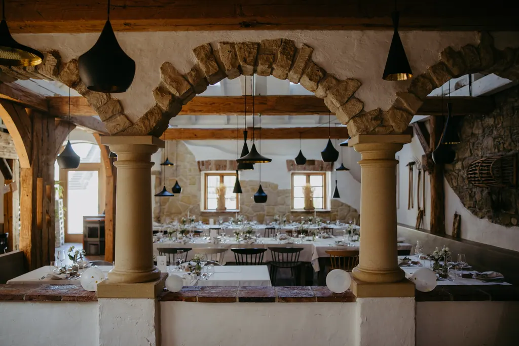Festsaal mit Steinbögen, Säulen, Holzbalken und gedeckten Tafeln