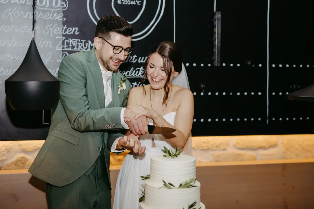 Brautpaar schneidet lachend die weiße Hochzeitstorte an