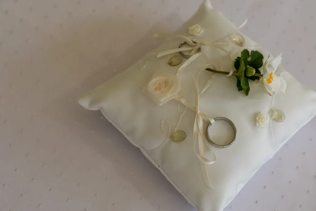 Zwei Eheringe auf einem cremefarbenen Ringkissen mit Blüten