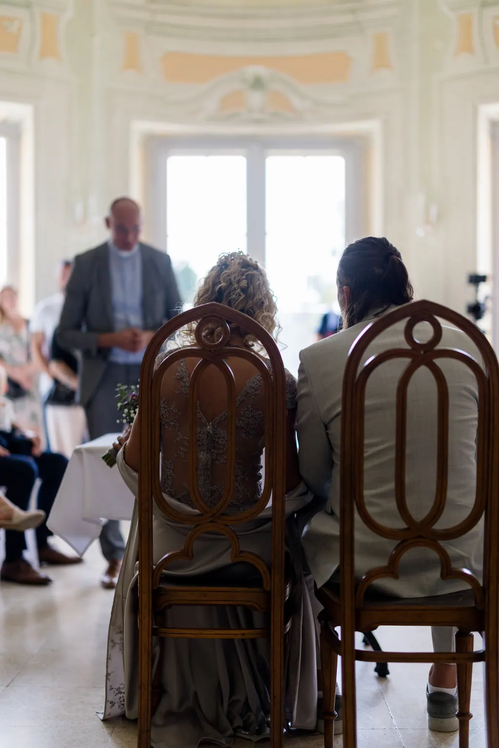 Brautpaar sitzt während der Zeremonie im Saal der Orangerie, von hinten gesehen