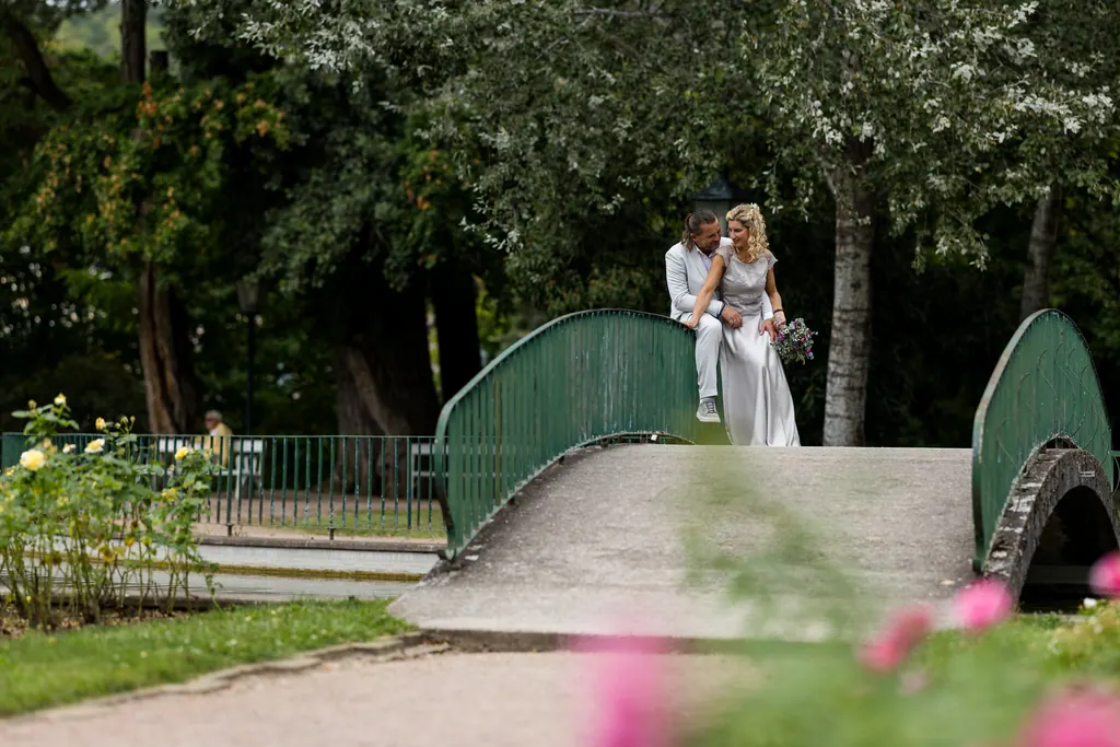 Brautpaar auf einer grünen Bogenbrücke im Park, unscharfe Rosen im Vordergrund
