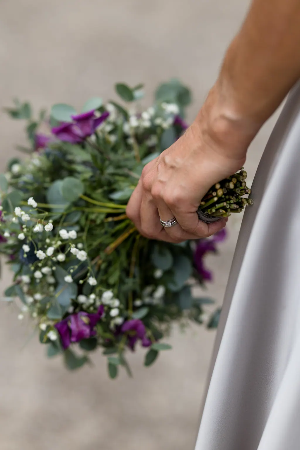 Hand der Braut mit Ehering am Brautstrauß aus Disteln und Schleierkraut
