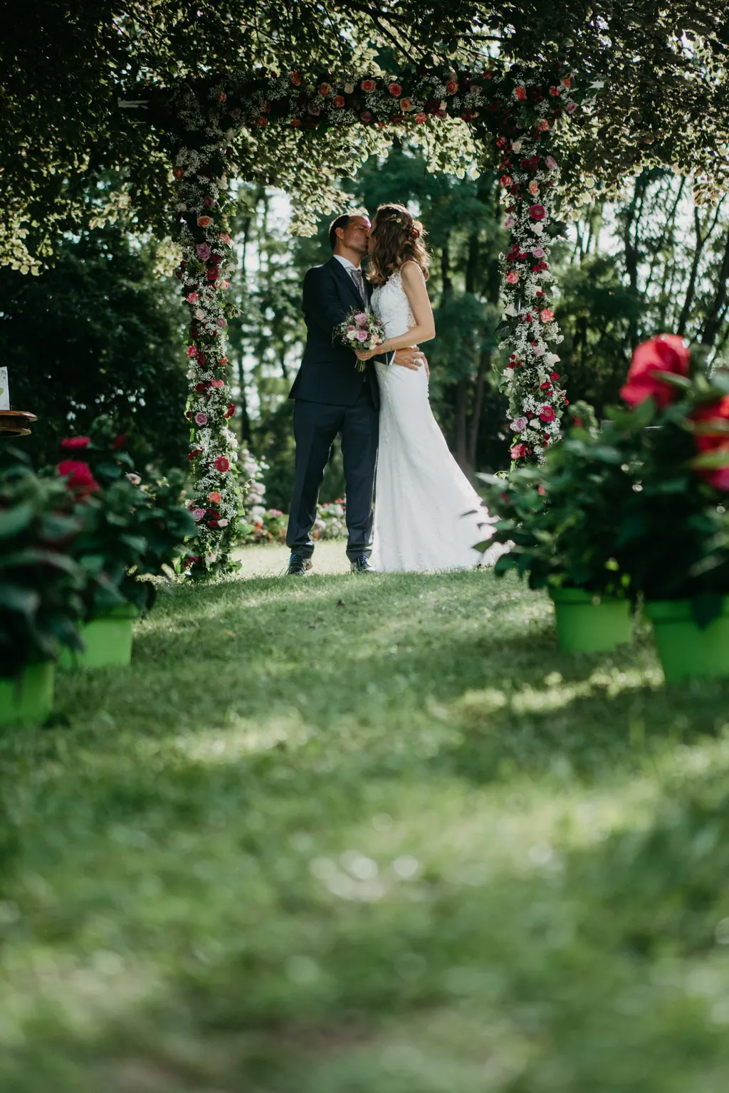 Brautpaar küsst sich unter dem Rosenbogen im Garten