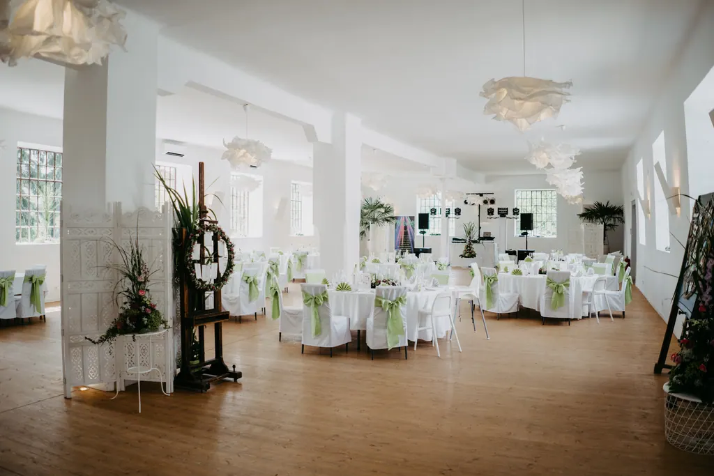 Heller Festsaal mit Holzboden, weißen Säulen und historischen Maschinen